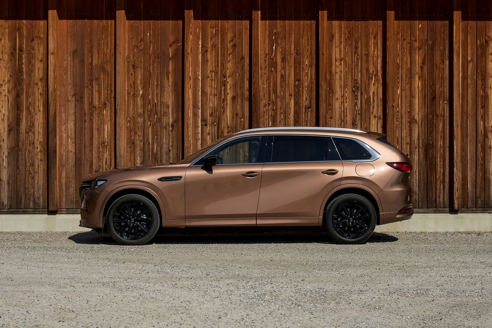 Copper coloured Mazda CX-80 in front of a wooden fence