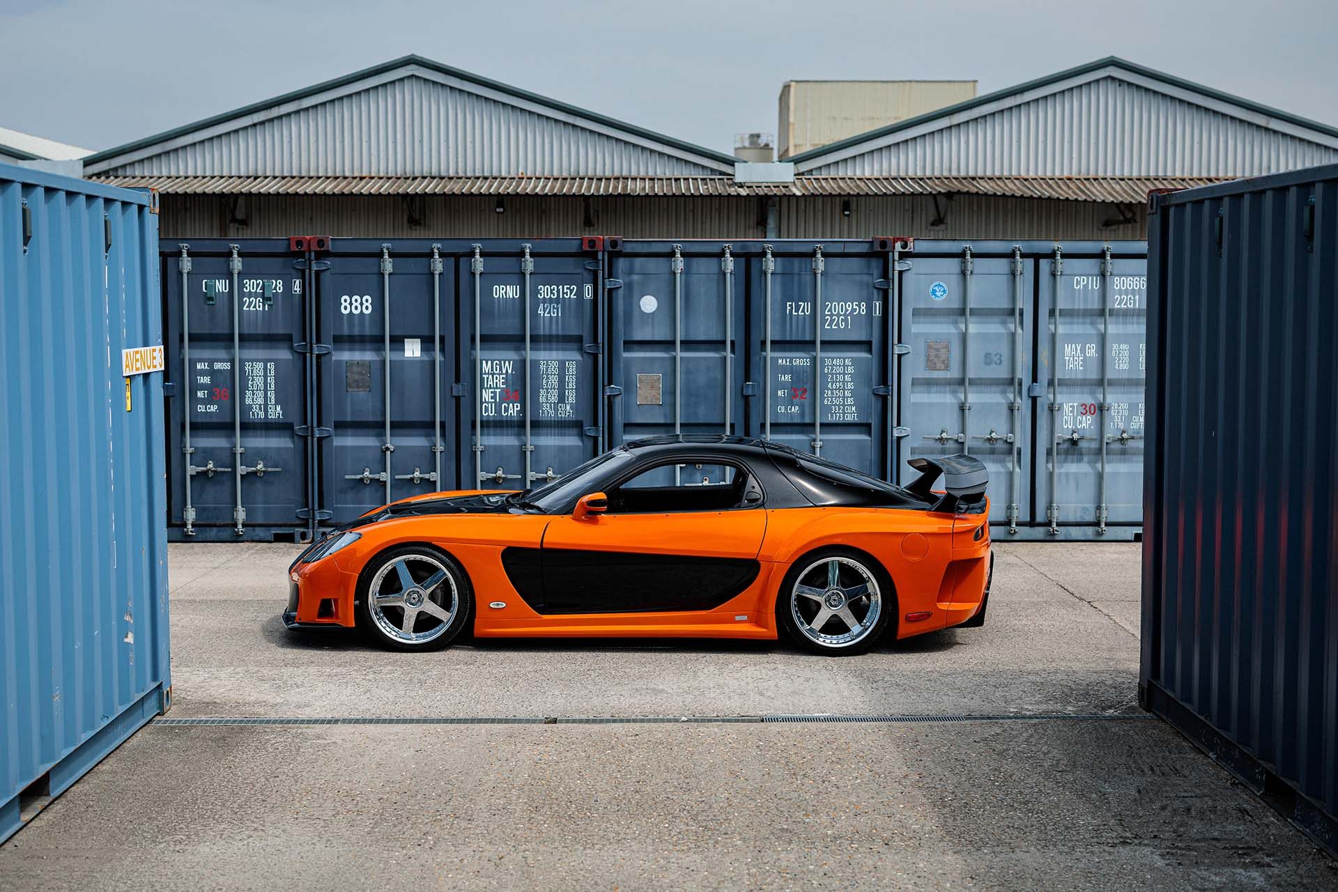 Fast and Furious Mazda RX-7 in orange in front of blue containers
